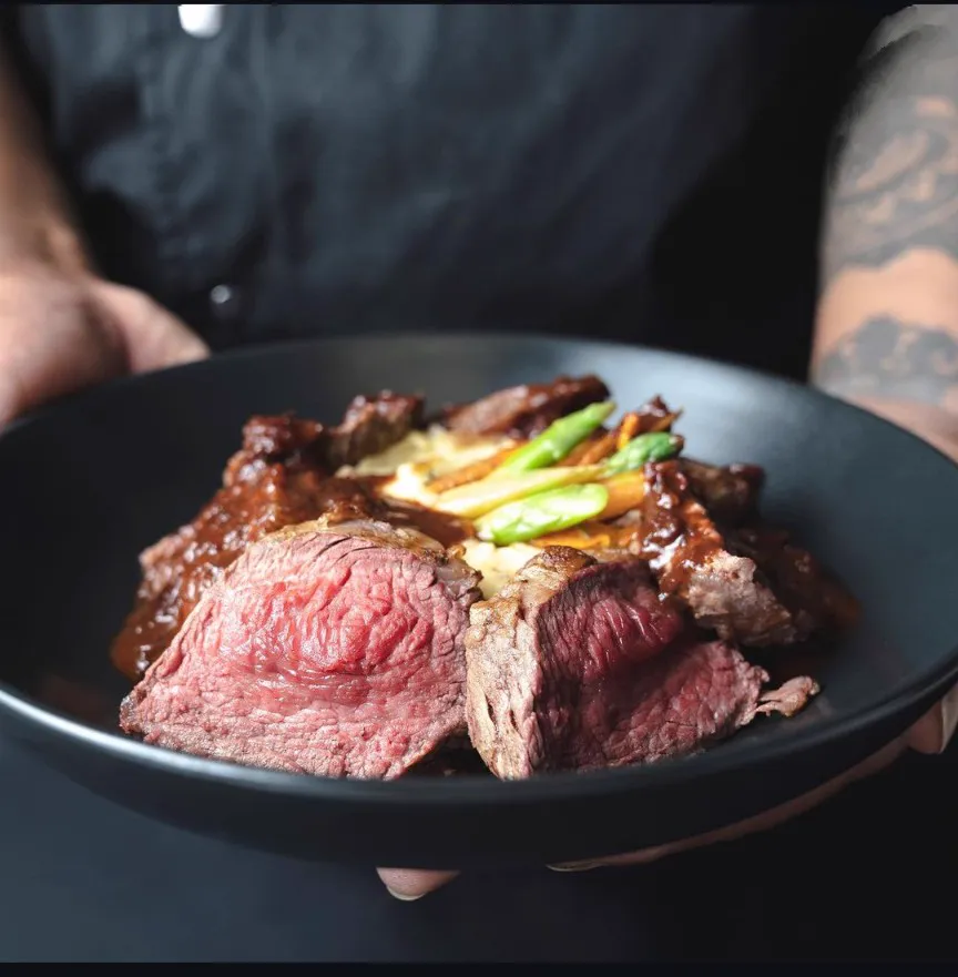 Sliced steak over a creamy base with asparagus in a black bowl